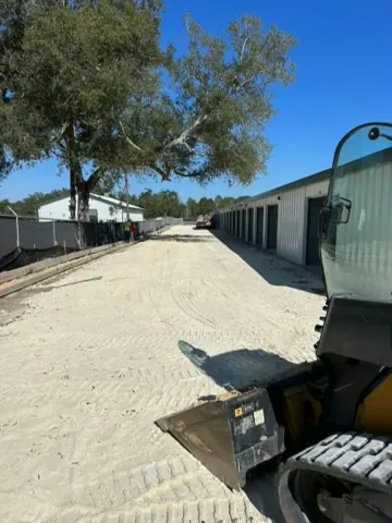 Compact track loader on a graded lane between buildings and oak trees