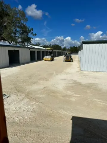 Wide graded sand and limerock yard between metal storage buildings