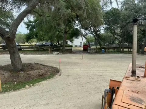 Graded dirt lot under large live oak trees viewed from the cab of a machine