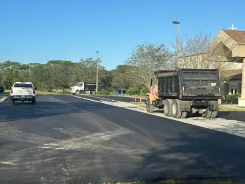 Dump truck and crew on a freshly paved drive beside a large building