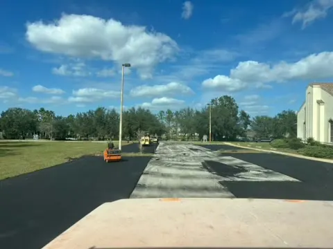 Paving in progress on a long drive with cones set out and light poles overhead