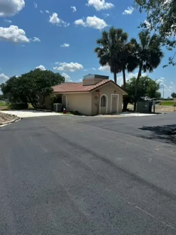 New asphalt drive sweeping past a small tile roofed building and open lawn