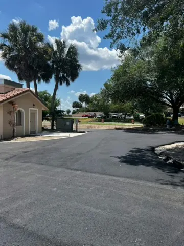 Fresh asphalt parking area edged by palm trees and a tile roofed building