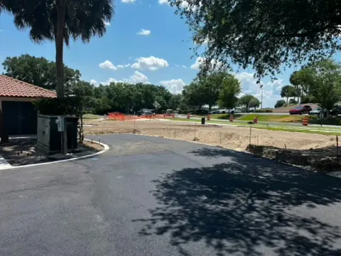 New asphalt drive and curb return beside a building with palms and fresh sod edges