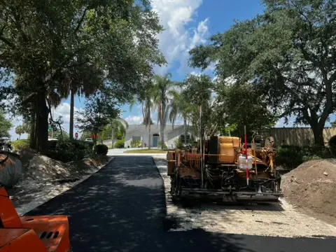 Asphalt paver laying a new mat of hot mix asphalt on a tree lined drive
