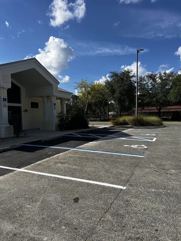 Striped parking lot with a blue accessible stall and access aisle beside a commercial building