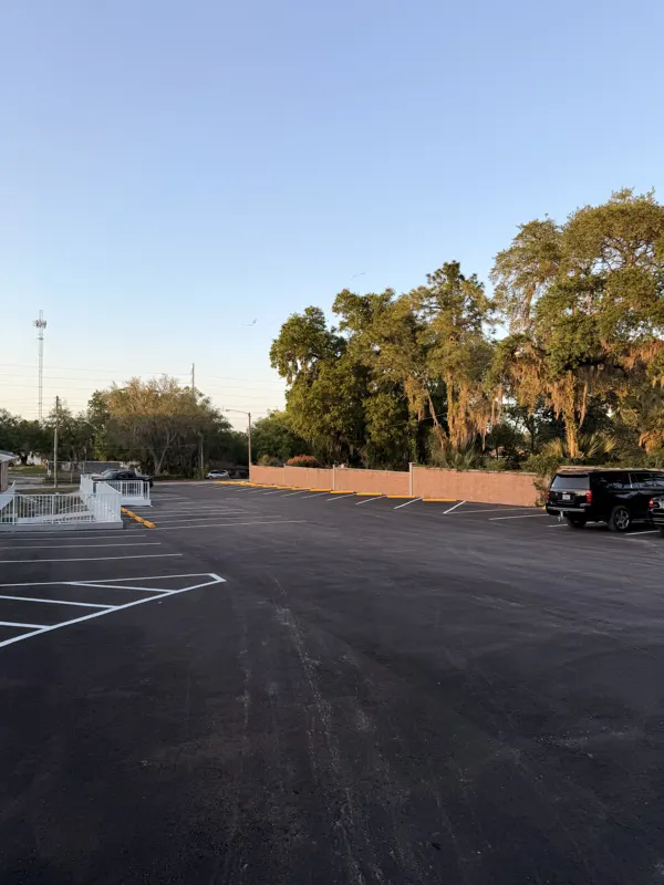 Newly paved commercial parking lot with a black pickup and oak trees behind a brick wall