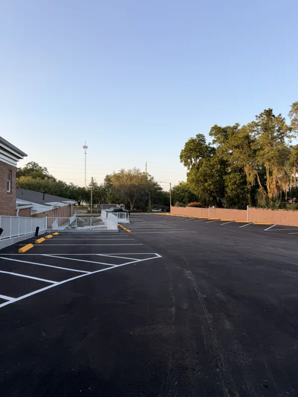 New asphalt parking lot with white stall lines and yellow curb paint beside a building