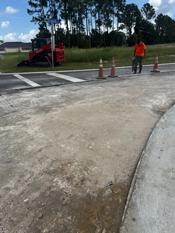 Prepared base at a road entrance with a compact track loader and a worker setting cones