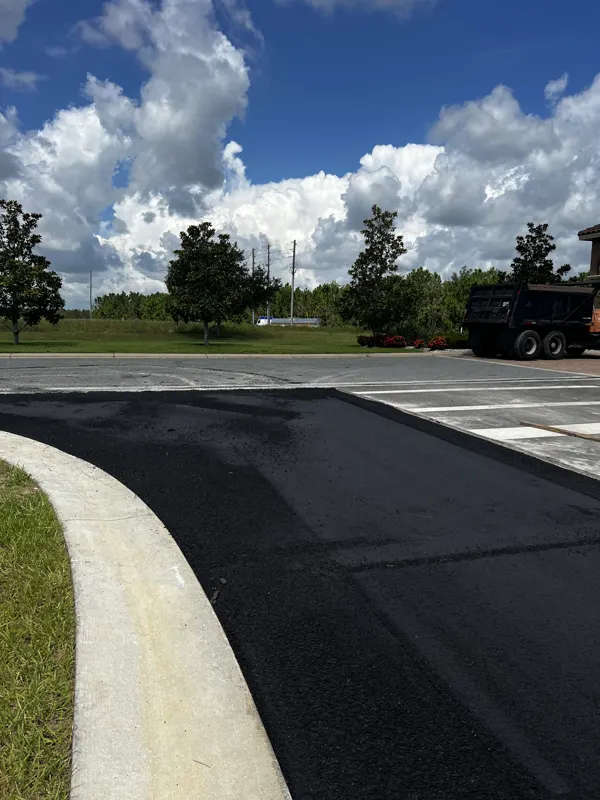 New asphalt meeting a curved concrete curb at a road entrance