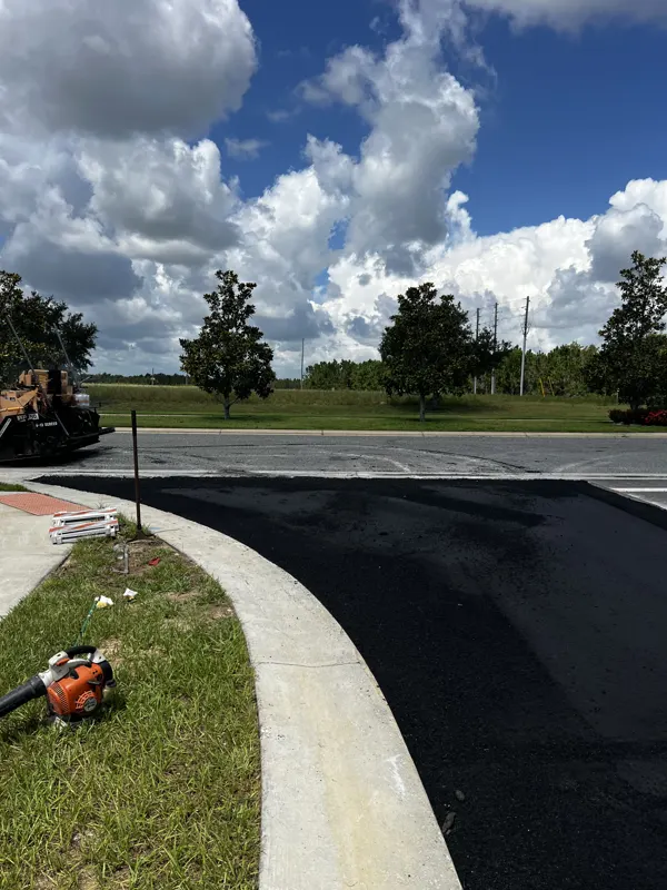 Fresh asphalt along a curved curb with a dump truck and roller in the background