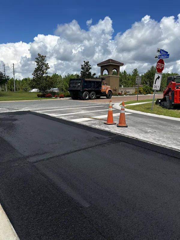 Fresh asphalt at a road entrance with an entry tower, dump truck and cones