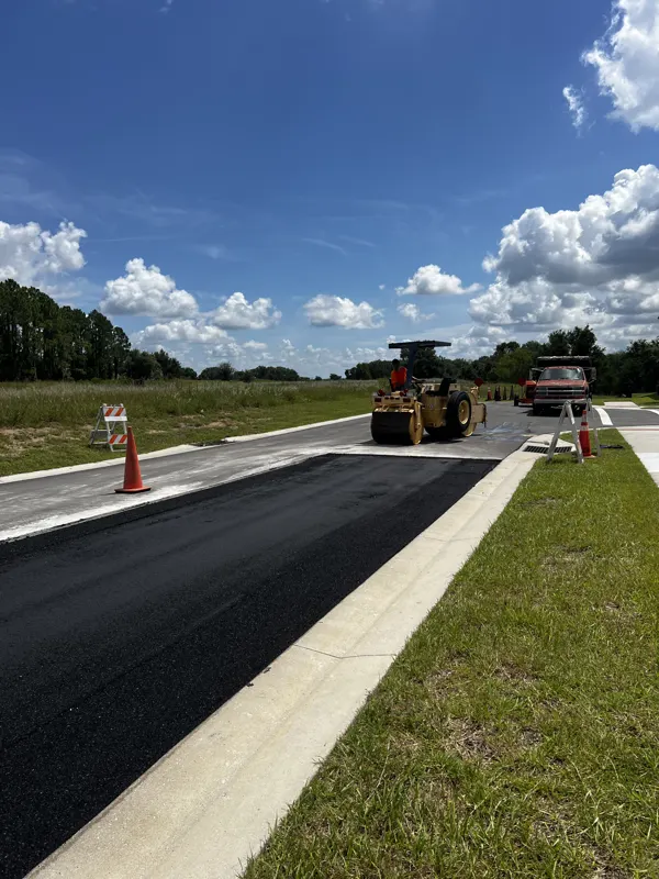 Roller compacting new asphalt along a curb at a road entrance