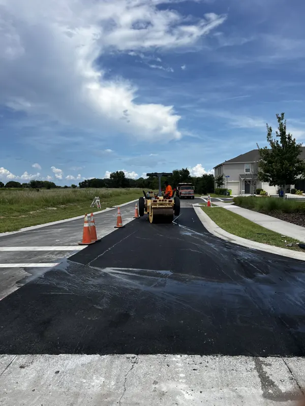 Roller and crew working a fresh asphalt entrance with a house in the background