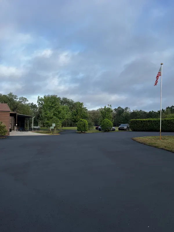 Wide new asphalt motor court with a flagpole and trees