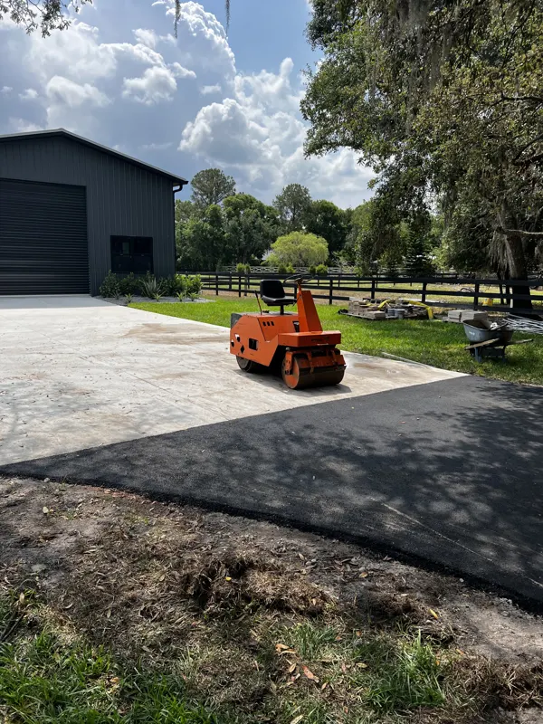 Small roller on a new asphalt driveway beside a gray garage building