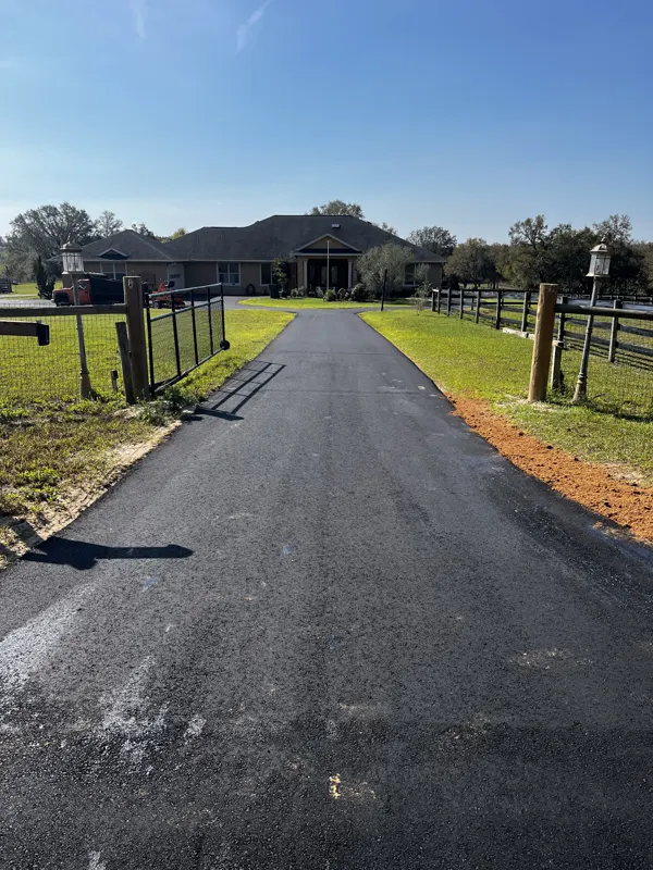 Long new asphalt driveway running through a ranch gate toward a house