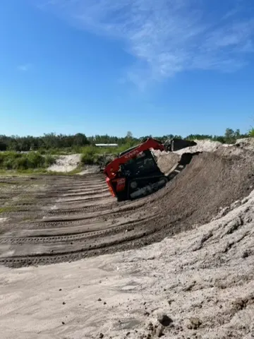 Compact track loader moving a large pile of dirt on an open site